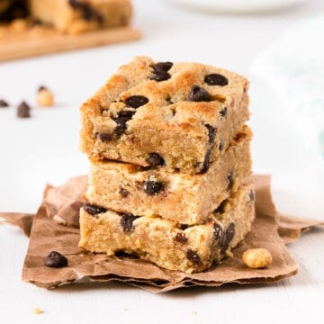 chocolate peanut butter bars stacked on top of each other on parchment paper, with a cup of coffee in the background.