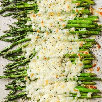 a baking sheet lined with parchment paper, full of roasted asparagus, garlic and melted cheese.