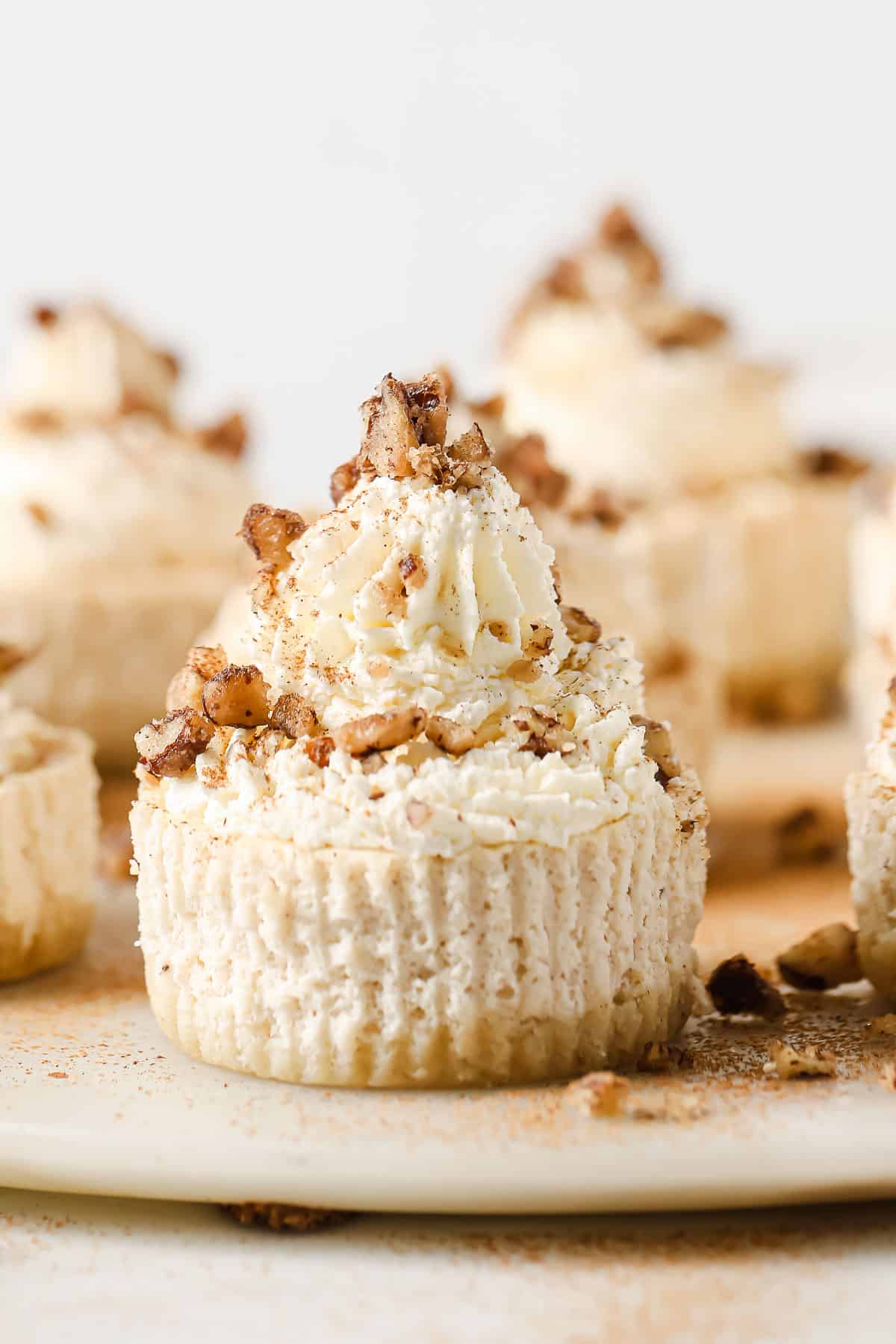 A serving platter with mini cheesecakes, topped with whipped cream and candied nuts.